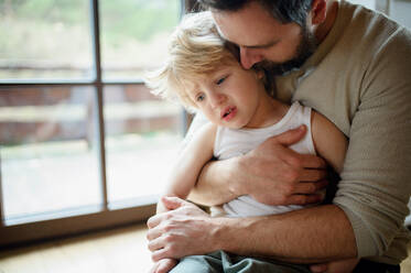 Father with small sick unhappy son indoors at home, holding and comforting him. - HPIF16532