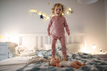 Vorderansicht eines kleinen Kleinkindes, das zu Hause auf dem Bett herumspringt und Spaß hat. - HPIF16545