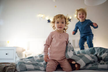 Zwei kleine lachende Kinder, die zu Hause auf dem Bett herumspringen und Spaß haben. - HPIF16548