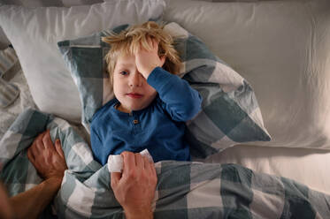 Unbekannter Vater, der nach seinem kleinen kranken Sohn sieht, der zu Hause im Bett liegt. - HPIF16555
