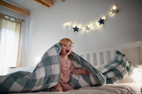 Kleines Kleinkind Mädchen spielt und versteckt sich auf dem Bett zu Hause, Spaß haben. - HPIF16556