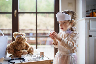 Kleines Kleinkind Mädchen mit Arzt Uniform drinnen zu Hause, spielen mit Teddybär. - HPIF16563