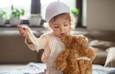 Kleines Kleinkind Mädchen mit Arzt Uniform drinnen zu Hause, spielen mit Teddybär. - HPIF16569