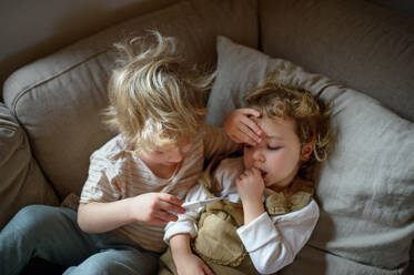 Zwei kleine kranke Kinder, Bruder und Schwester, liegen zu Hause im Bett und messen die Temperatur. - HPIF16575