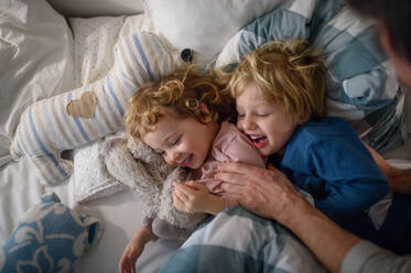 Zwei fröhliche kleine lachende Kinder mit unerkennbarem Vater, die sich zu Hause amüsieren. - HPIF16586