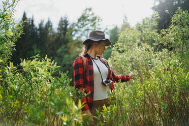 Vorderansicht einer jungen Frau mit Kamera auf einem Waldspaziergang in sommerlicher Natur. - HPIF16607