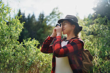 Seitenansicht einer jungen Frau mit einem Hund bei einem Spaziergang in der sommerlichen Natur, beim Fotografieren. - HPIF16610