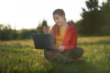 A happy young woman using laptop outdoors in summer nature, video call concept. - HPIF16632