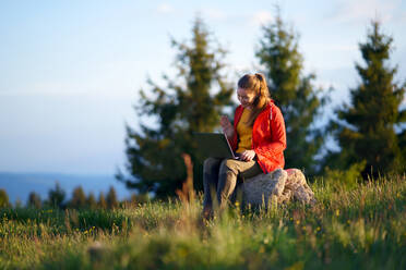 Eine glückliche junge Frau mit Laptop im Freien im Sommer Natur, Videoanruf Konzept. - HPIF16633