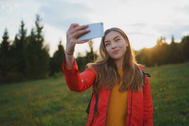 Side view of young woman on a walk outdoors on meadow in summer nature, taking selfie. - HPIF16644