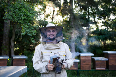 Porträt eines Imkers, der in einem Bienenhaus arbeitet und einen Bienenräucherschrank hält. - HPIF16699