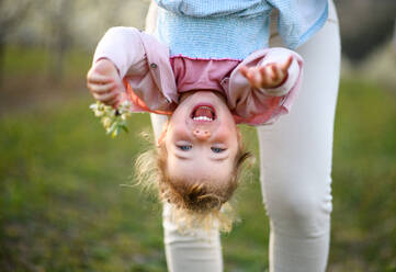 Unerkennbare Mutter hält fröhliche kleine Tochter kopfüber im Freien im Frühling Natur. - HPIF16716