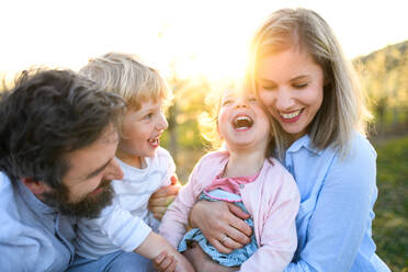 Vorderansicht einer Familie mit zwei kleinen Kindern, die bei Sonnenuntergang im Freien in der Natur lachen. - HPIF16727