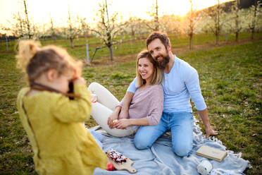 Kleines Mädchen mit Kamera fotografieren Familie auf Picknick im Freien im Frühjahr Natur bei Sonnenuntergang. - HPIF16732