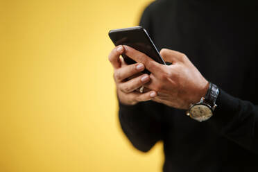 Midsection of man with smartphone in a studio on yellow background. Copy space. - HPIF16736