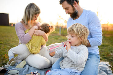 Front view of family with two small children having picnic outdoors in spring nature at sunset. - HPIF16763