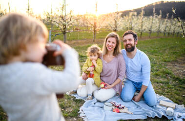 Kleiner Junge mit Kamera fotografiert Familie beim Picknick im Freien im Frühling Natur bei Sonnenuntergang. - HPIF16766