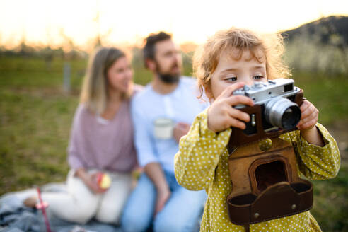 Kleines Mädchen mit Kamera fotografieren Familie auf Picknick im Freien im Frühjahr Natur bei Sonnenuntergang. - HPIF16768