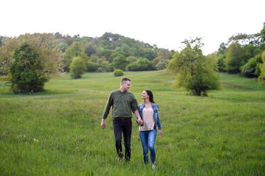 Verliebtes, glückliches Paar, das in der Natur spazieren geht und sich an den Händen hält. - HPIF16792