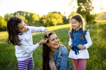 Front view of mother with two small daughters having fun outdoors in spring nature, putting flowers in hair. - HPIF16800