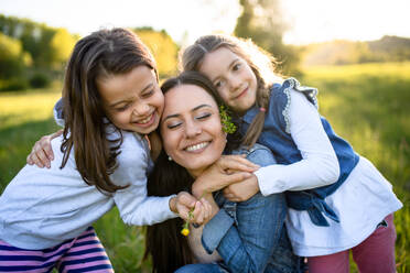 Front view of mother with two small daughters having fun outdoors in spring nature, hugging. - HPIF16801