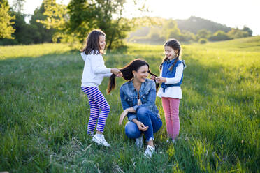 Vorderansicht einer Mutter mit zwei kleinen Töchtern, die sich in der frühlingshaften Natur vergnügen und mit den Haaren spielen. - HPIF16802