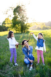 Vorderansicht einer Mutter mit zwei kleinen Töchtern, die sich in der frühlingshaften Natur vergnügen und mit den Haaren spielen. - HPIF16803