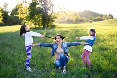 Front view of mother with two small daughters having fun outdoors in spring nature, pulling hair. - HPIF16804