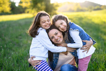 Vorderansicht einer Mutter mit zwei kleinen Töchtern, die sich im Frühling in der Natur vergnügen und sich umarmen. - HPIF16805