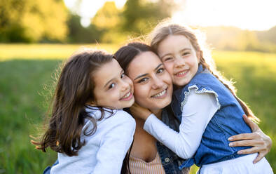 Vorderansicht einer Mutter mit zwei kleinen Töchtern, die sich im Frühling in der Natur vergnügen und sich umarmen. - HPIF16806