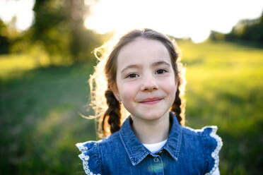 Front view portrait of small girl standing outdoors in spring nature, looking at camera. - HPIF16808