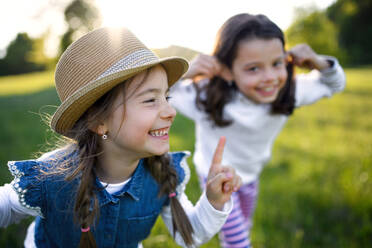 Front view portrait of two small girls standing outdoors in spring nature, laughing. - HPIF16813