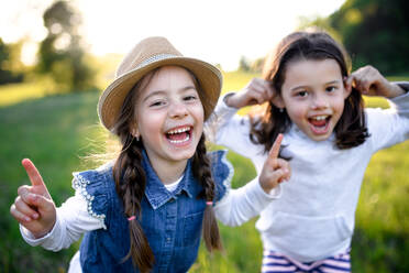 Front view portrait of two small girls standing outdoors in spring nature, laughing. - HPIF16814