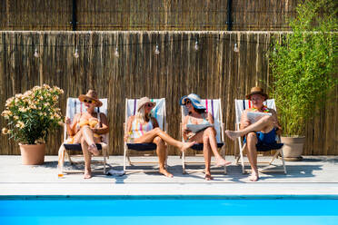 Eine Gruppe fröhlicher Senioren sitzt am Swimmingpool im Hinterhof und entspannt sich. - HPIF16819