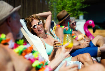 Group of cheerful seniors sitting by swimming pool outdoors in backyard, a party concept. - HPIF16826
