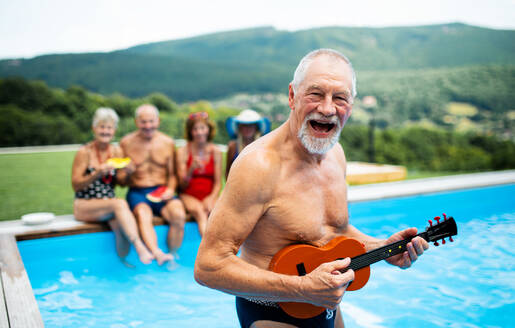 Gruppe von fröhlichen Senioren mit Gitarre am Swimmingpool im Freien im Hinterhof, ein Partykonzept. - HPIF16851