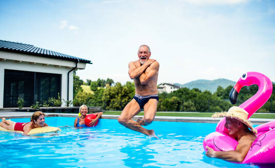 Group of cheerful seniors in swimming pool outdoors in backyard, jumping in water. - HPIF16856