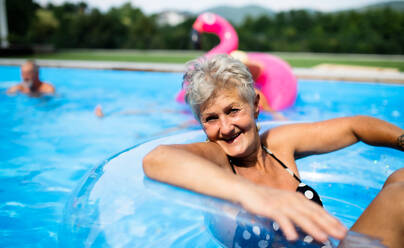 Portrait of senior woman in swimming pool outdoors in backyard, looking at camera. Copy space. - HPIF16857