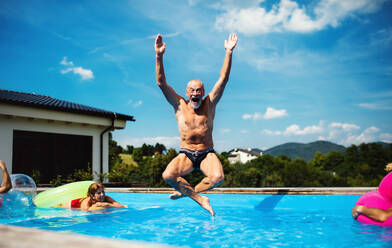 Group of cheerful seniors in swimming pool outdoors in backyard, jumping in water. - HPIF16859