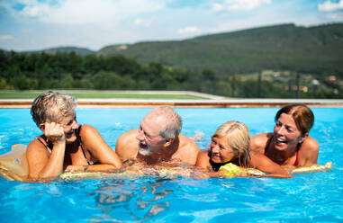 Eine Gruppe fröhlicher Senioren im Schwimmbad im Hinterhof, die sich entspannen und unterhalten. - HPIF16864