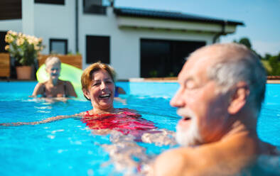 A group of cheerful seniors in swimming pool outdoors in backyard, having fun. - HPIF16867