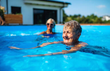 Portrait of senior woman with friends in swimming pool outdoors in backyard. - HPIF16872