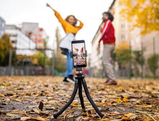 Portrait of young couple with smartphone making video for social media outdoors in park. - HPIF16894