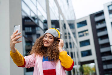 Portrait of young woman with smartphone making video for social media outdoors on street. - HPIF16899