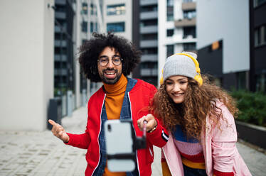 Porträt eines jungen Paares mit Smartphone, das draußen auf der Straße ein Video für soziale Medien dreht. - HPIF16901