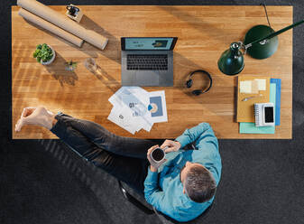 Top view of relaxing businessman working on computer at desk with paperwork and coffee in home office. - HPIF16919