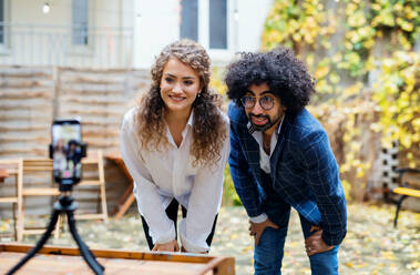 Portrait of young couple with smartphone making video for social media outdoors in park. - HPIF16931