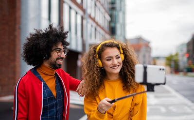 Porträt eines jungen Paares mit Smartphone, das draußen auf der Straße ein Video für soziale Medien dreht. - HPIF16939