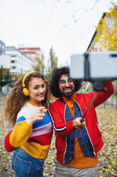 Portrait of young couple with smartphone making video for social media outdoors in city park. - HPIF16944