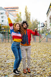 Porträt eines jungen Paares mit Smartphone, das im Freien im Park ein Video für soziale Medien aufnimmt. - HPIF16945